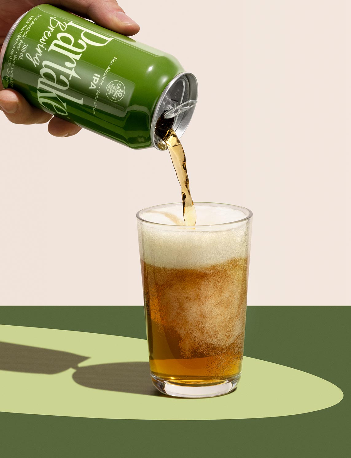 A green can of Partake Brewing non-alcoholic IPA, with a 10 calories badge, being poured into a clear glass